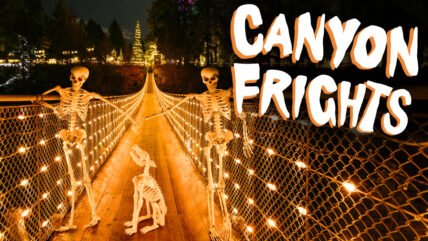 Skeletons cast eerie silhouettes against the night sky as they traverse the Capilano Suspension Bridge during Canyon Frights, with the bridge illuminated in haunting orange, adding a spooky ambiance to the Halloween festivities