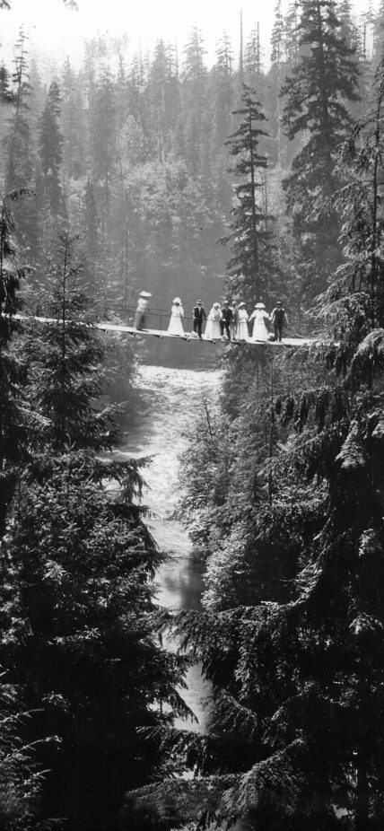 A historical black and white photo captures a wedding party on the first Capilano Suspension Bridge in 1889, offering a glimpse into the bridge's early days and its significance as a landmark for celebrations and gatherings