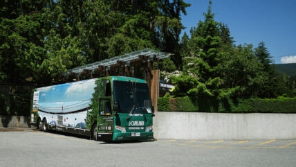 A free shuttle bus parked in the lot at Capilano Suspension Bridge Park, ready to transport visitors to the entrance of the park, surrounded by trees and foliage on a sunny day